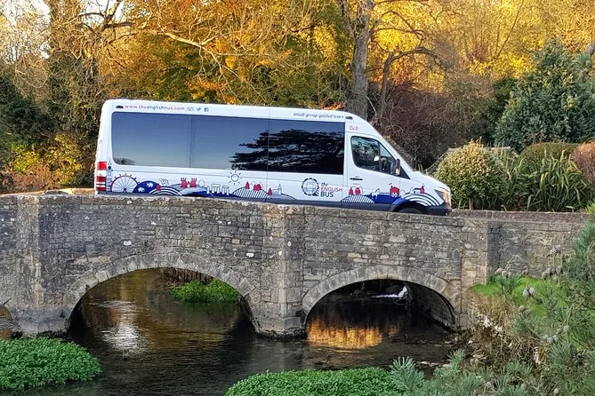 A minibus crossing an old stone bridge in a Cotswold village
